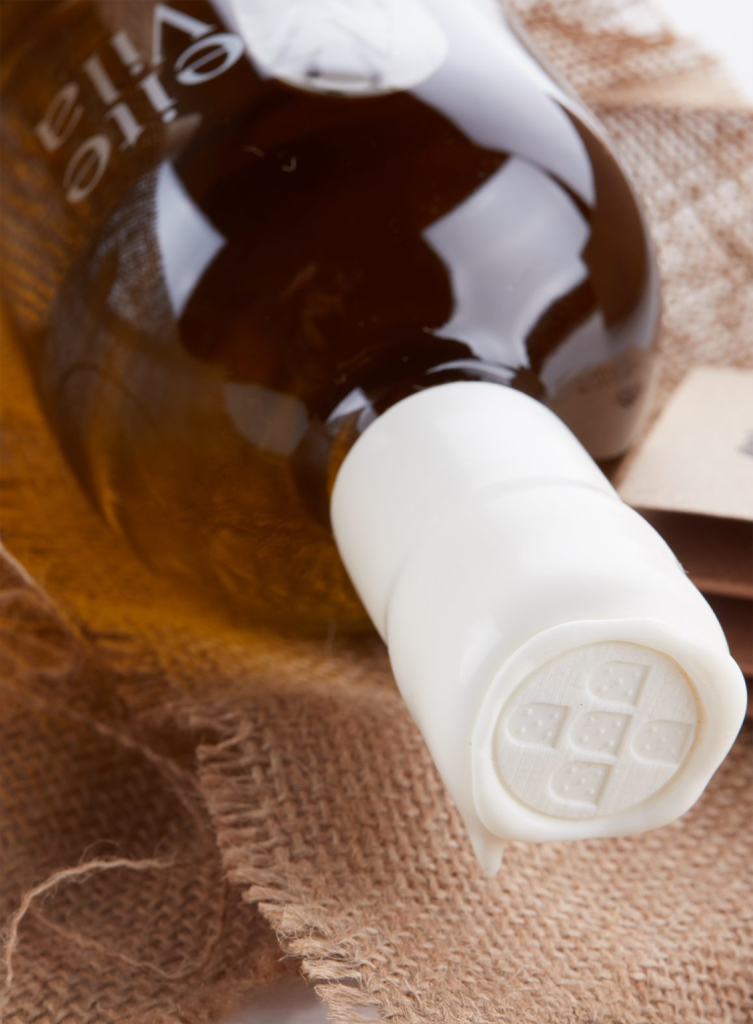 Close-up of the white wax seal on an Azeite Da Vila olive oil bottle, featuring a traditional Portuguese symbol embossed on top, resting on rustic jute fabric.