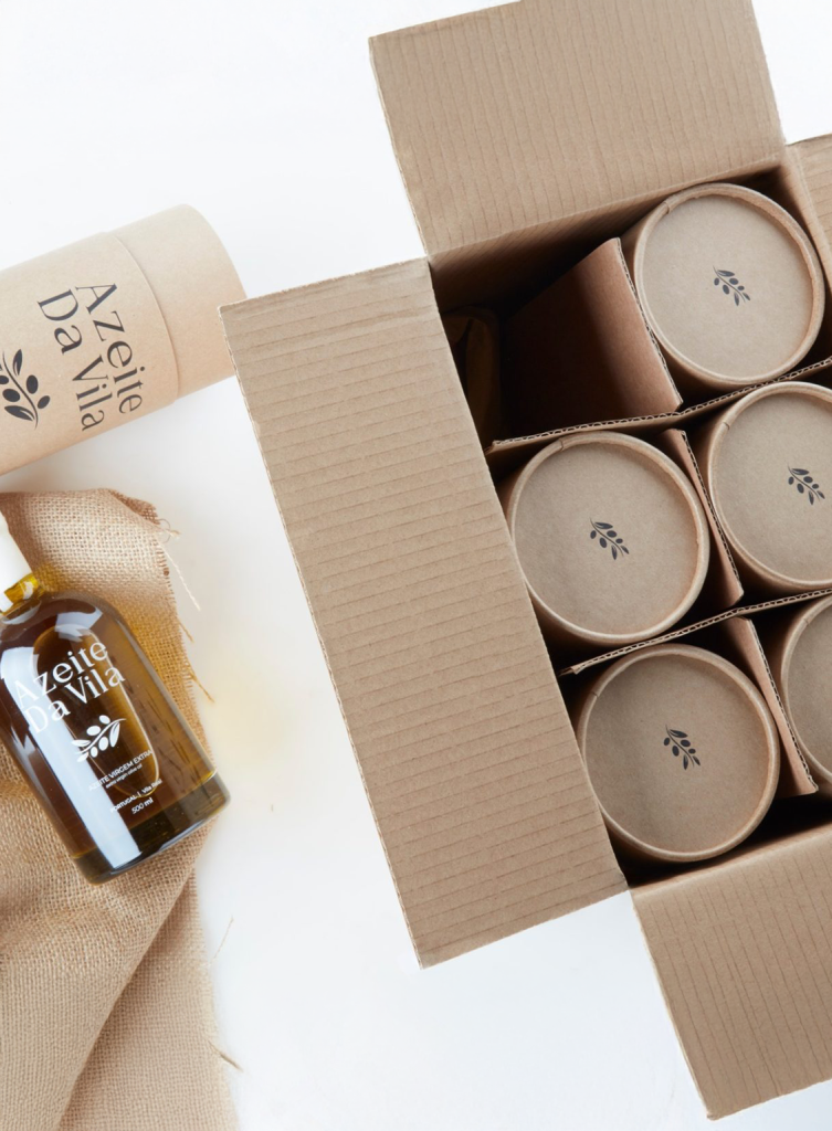 Cardboard shipping box containing six eco-friendly paper tubes of Azeite Da Vila olive oil, alongside a single wax-sealed bottle on jute fabric.